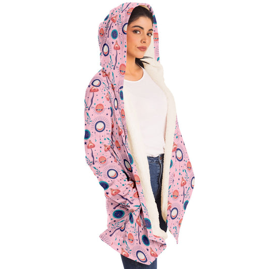 Woman wearing a cozy, hooded, pink microfleece cloak with a colorful, trippy mushroom design.