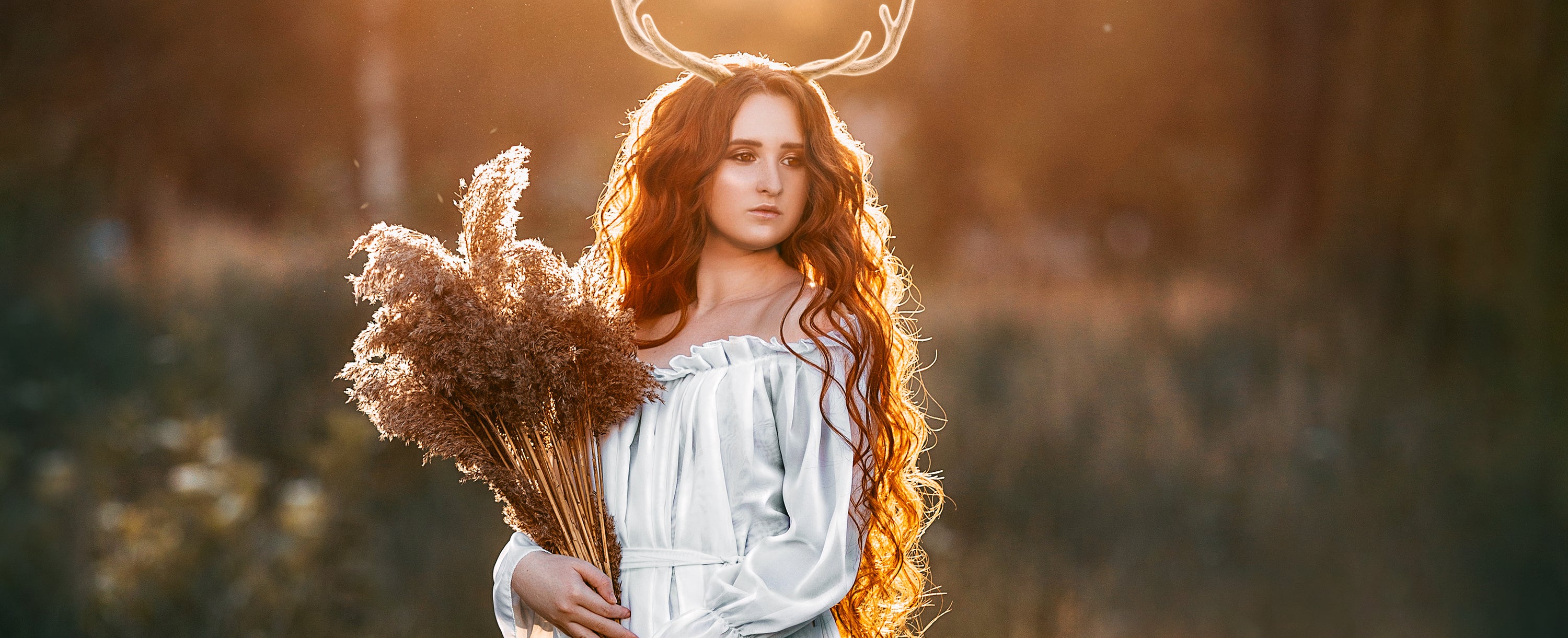 Woman with long red hair and antlers standing in a field with a fox.