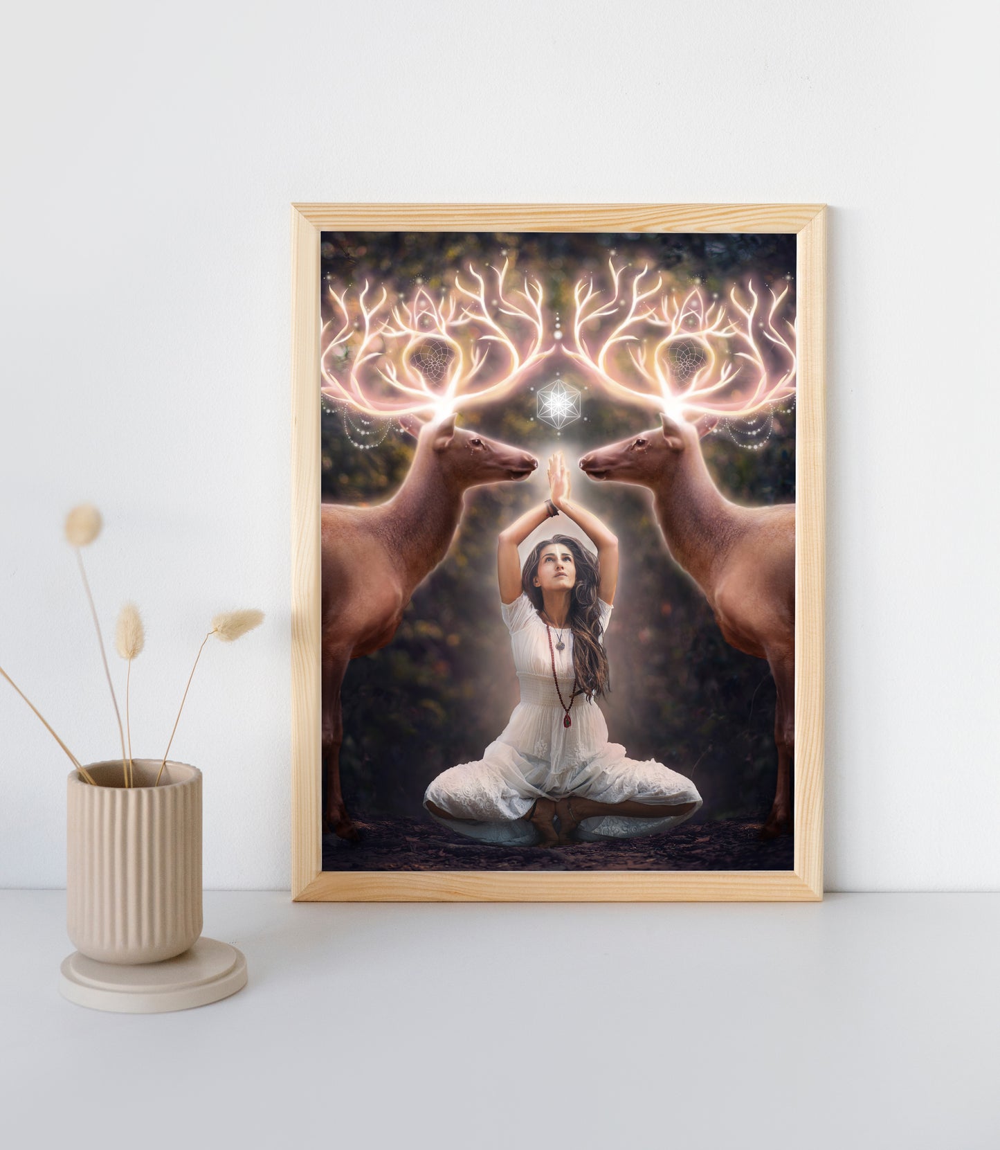 Two elk with glowing antlers stand on either side of a woman meditating in the forest.