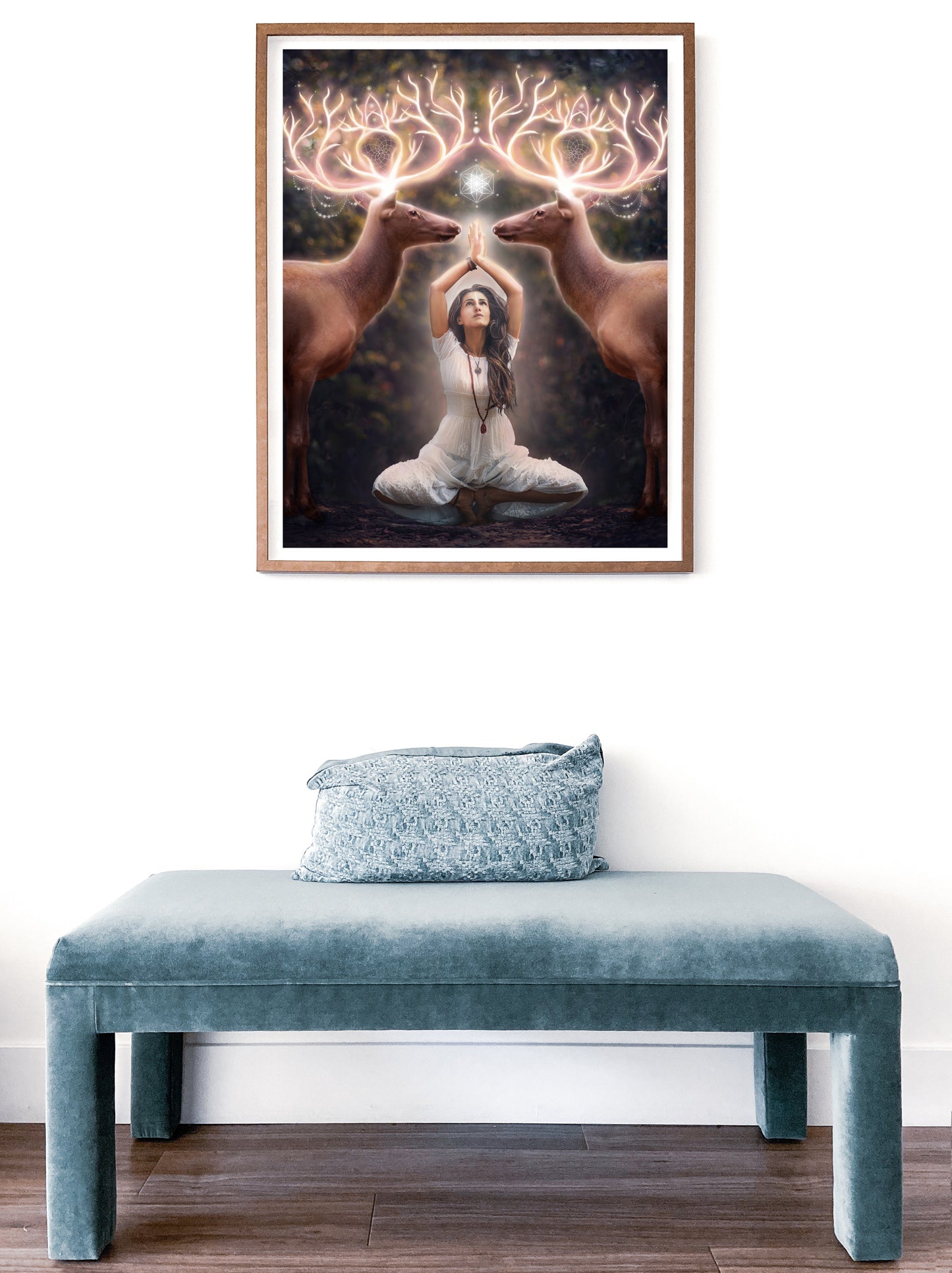 Two elk with glowing antlers stand on either side of a woman meditating in the forest.