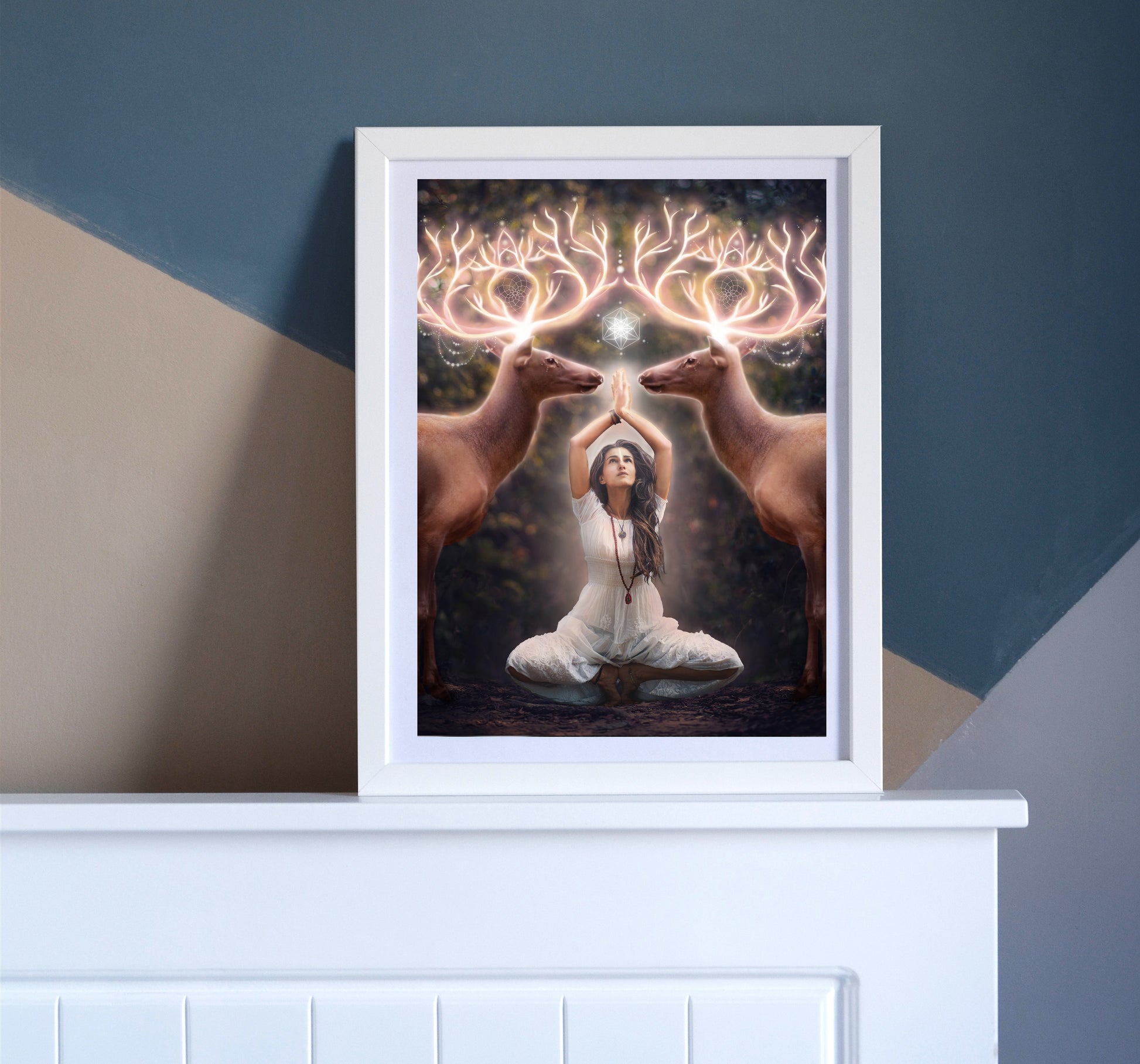 Two elk with glowing antlers stand on either side of a woman meditating in the forest.
