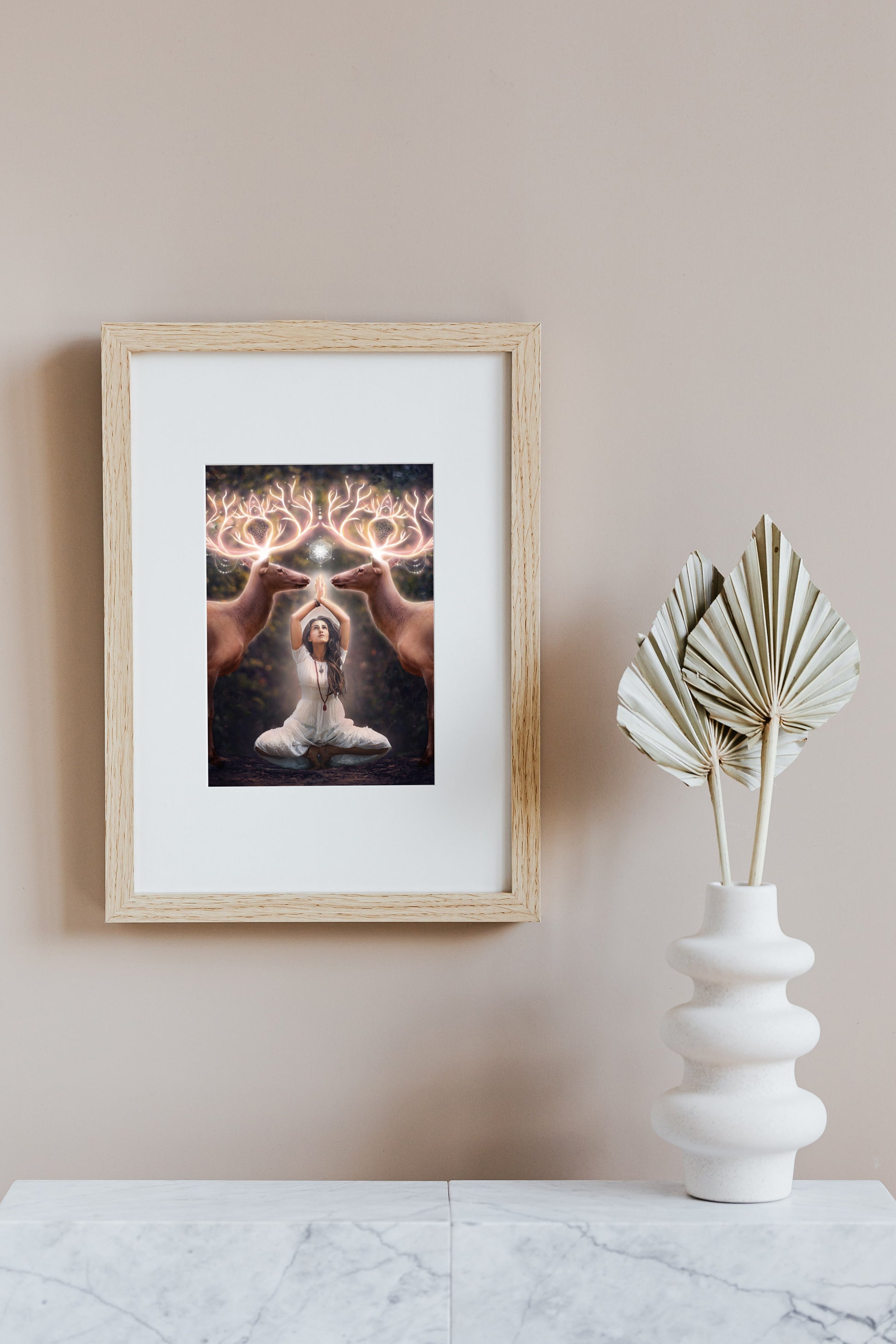 Two elk with glowing antlers stand on either side of a woman meditating in the forest.